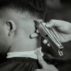 Detailed black and white close-up of a barber trimming a man's hair with clippers.